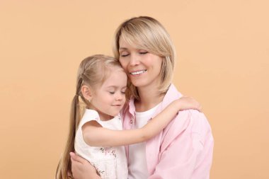 Daughter hugging her happy mother on beige background