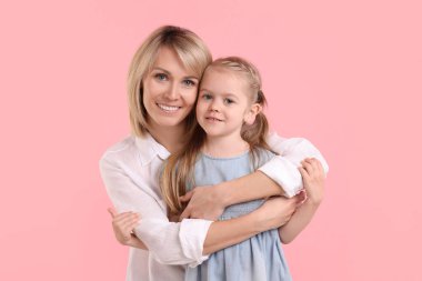 Mother hugging her happy daughter on pink background