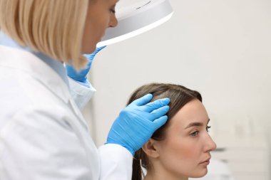 Trikoloğum klinikte fenerin altında hastanın saçını inceliyor.