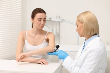 Dermatoskoplu bir dermatolog klinikteki hastayı muayene ediyor.