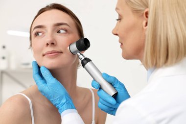 Dermatoskoplu bir dermatolog klinikte hastanın yüzünü inceliyor.