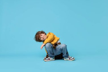 Mutlu küçük çocuk açık mavi arka planda dans ediyor