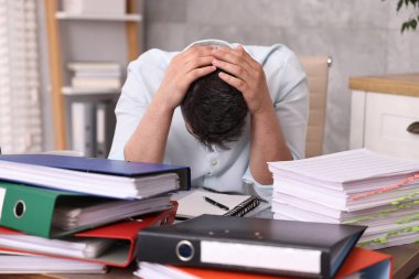 Ofisteki belgelerle çevrili bunalmış bir adam.