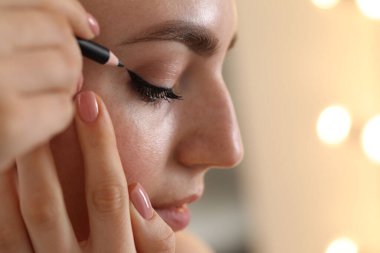 Makyaj ürünü. Kapalı alanda siyah göz kalemi kullanan kadın, yakın plan.