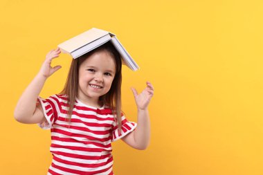 Turuncu arka plan üzerine açık kitabı olan sevimli küçük bir kız. Metin için boşluk