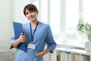 Portrait of smiling medical assistant with clipboard and pen in hospital. Space for text