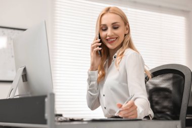 Sekreter ofiste akıllı telefondan konuşuyor.