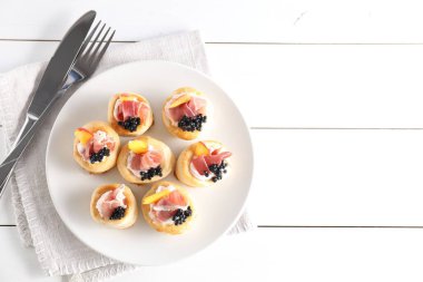 Krem peynirli, jambonlu, havyarlı, şeftalili ve çatallı hamur tatlısı beyaz ahşap masa, üst manzara. Metin için boşluk