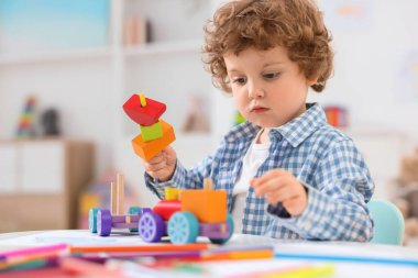Anaokulunda beyaz masada tahta oyuncaklarla oynayan sevimli küçük çocuk.