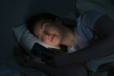 Woman using smartphone on bed at night. Internet addiction