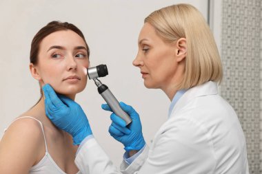 Dermatoskoplu bir dermatolog klinikte hastanın yüzünü inceliyor.