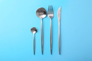 Açık mavi masaya dizilmiş şık çatal bıçak takımı, düz.