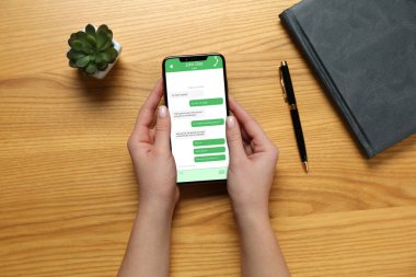 Ahşap masada cep telefonuyla mesajlaşan bir kadın. İletili aygıt ekranı