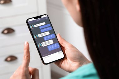 Kapalı alanda cep telefonuyla mesajlaşan bir kadın, yakın çekim. İletili aygıt ekranı