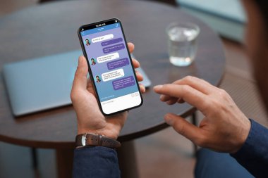 Kapalı mekanda cep telefonuyla mesajlaşan adam, yakın çekim. İletili aygıt ekranı