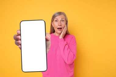 Altın arka planda boş ekranlı cep telefonu gösteren olgun bir kadın. Tasarım için model