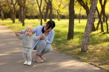 Anne, o dışarıda yürümeyi öğrenirken bebeğine bakıyor.