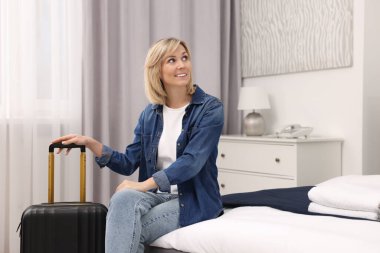 Şık bir otel odasında bavulla gülümseyen bir misafir.
