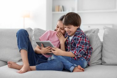 Evdeki kanepede tabletli mutlu erkek ve kız kardeşler.