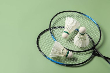 Yeşil arka planda badminton mekikleri ve raketler var. Metin için boşluk