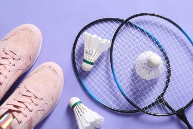 Tüy badminton mekik horozları, raketler ve spor ayakkabıları menekşe arka planda, düz yatıyordu