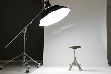 Modern stüdyoda beyaz fotoğraf, tabure ve profesyonel ışıklandırma ekipmanları