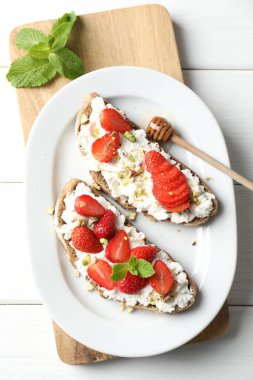 Çilekli, naneli ve şam fıstıklı nefis ricotta bruschetalar. Beyaz ahşap masada bal ile servis edilir.