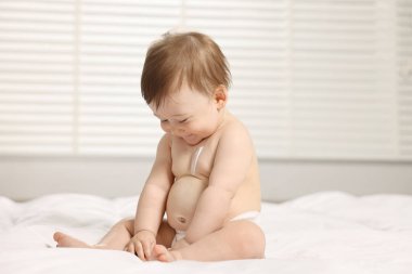 Vücuduna nemlendirici krem sürmüş tatlı küçük bebek evde yatakta oturuyor.