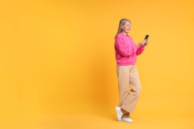 Turuncu arka planda telefonu olan son sınıf öğrencisi kadın, mesaj için yer var.