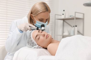 Dermatoskoplu bir dermatolog klinikte hastanın yüzünü inceliyor.