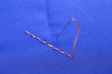 Dikiş iğnesi iplik ve dikişler mavi kumaş üzerinde, yakın çekim