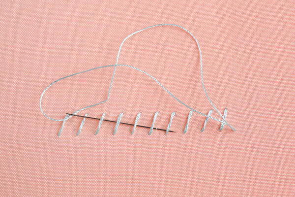 Sewing needle with thread and stitches on coral cloth, top view