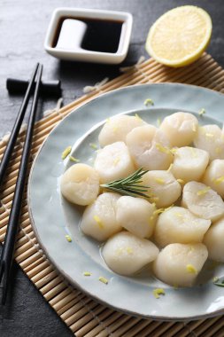 Limonlu çiğ deniz tarağı, biberiye ve soya sosu koyu dokulu masa, yakın plan.