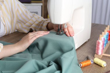 Terzi kadın, ahşap masada dikiş makinesiyle çalışıyor.