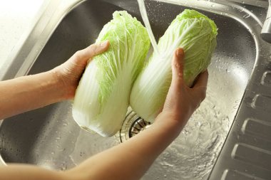 Woman washing fresh Chinese cabbages in sink, closeup