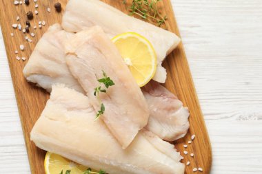 Çiğ morina balığı parçaları, beyaz ahşap masada limon ve baharatlar.