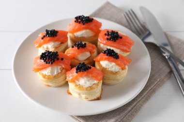 Krem peynirli lezzetli puf böreği, somon, siyah havyar ve beyaz ahşap masada çatal bıçak.