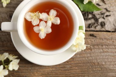 Aromatik yasemin çayı fincanda, çiçekler ve kuru yapraklar ahşap masada, üst manzara