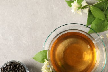 Aromatik yasemin çayı bardakta, çiçekler ve kuru yapraklar açık gri masada, düz yerde. Metin için boşluk