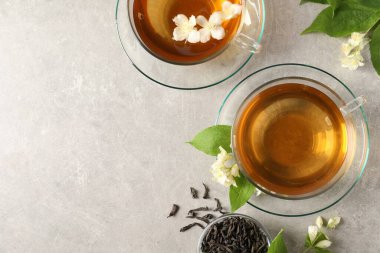 Aromatik yasemin çayı fincanlarda, çiçekler ve açık gri masada kuru yapraklar, düz yerde. Metin için boşluk