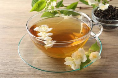 Aromatik yasemin çayı fincanda, çiçekler ve yapraklar ahşap masada