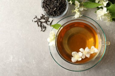 Aromatik yasemin çayı bardakta, çiçekler ve yapraklar açık gri masada, düz yerde. Metin için boşluk