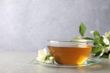 Aromatik yasemin çayı fincanda, çiçekler ve yeşil yapraklar açık gri masada, metin için boşluk