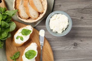 Krem peynirli lezzetli sandviçler ve ahşap masa üzerinde fesleğen yaprakları.