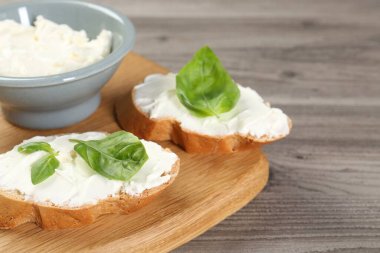 Krem peynirli ve fesleğenli lezzetli sandviçler ahşap masada, yakın plan.