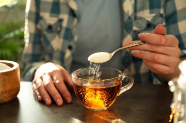 Koyu masada çay fincanına şeker koyan kadın, yakın plan.