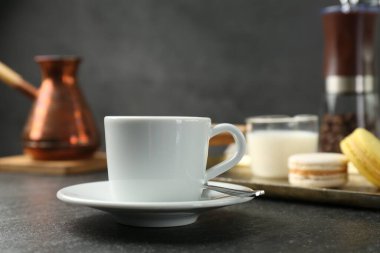 Beyaz espresso fincanı, kaşık ve çay tabağı koyu dokulu masa, yakın plan.