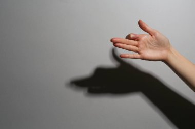 Gölge kuklası. Gri arka plandaki köpek gibi el hareketi yapan kadın, yakın plan. Metin için boşluk