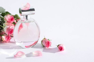 Bir şişe lüks parfüm ve beyaz arka planda güzel güller, yazı için yer. Çiçek kokusu.
