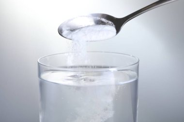 Açık gri arka planda su bardağına kabartma tozu eklemek, yakın plan